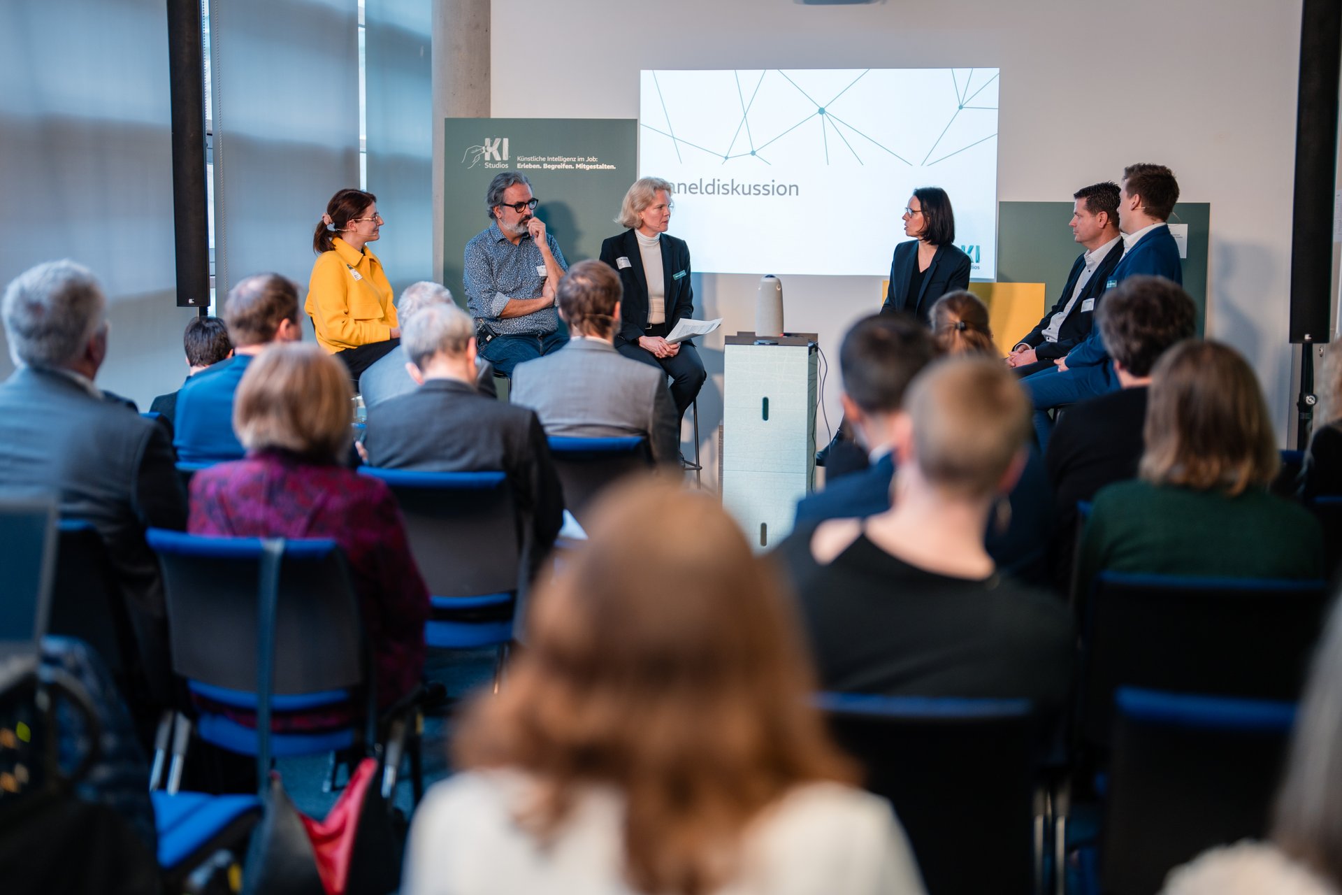 Zuschauer beobachten wie auf dem Panel Moderatorin Ana Dujić mit Thomas Kniehl, Rebecca Beiter und Carsten Gauch diskutiert